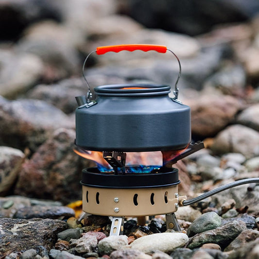Portable windproof camping gas stove with kettle on rocky outdoor surface for group cooking